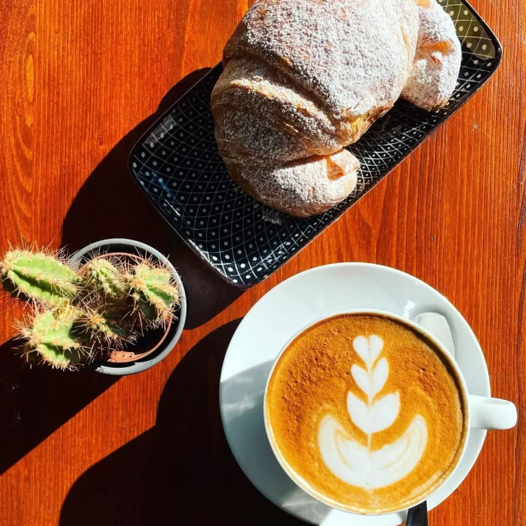 Cappuccino con latte art, croissant, brioche, su tavolo in legno per una colazione dolce all'Estro dalle 7.30 fino a tarda notte