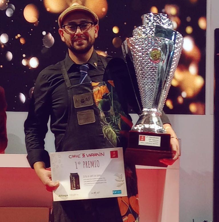 Gianluca Tofani, maestro del Caffè d'Italia 2023 Gianluca Tofani, maestro del Caffè d'Italia 2023 con cappellino e occhiali, tiene un trofeo e un certificato di primo premio.